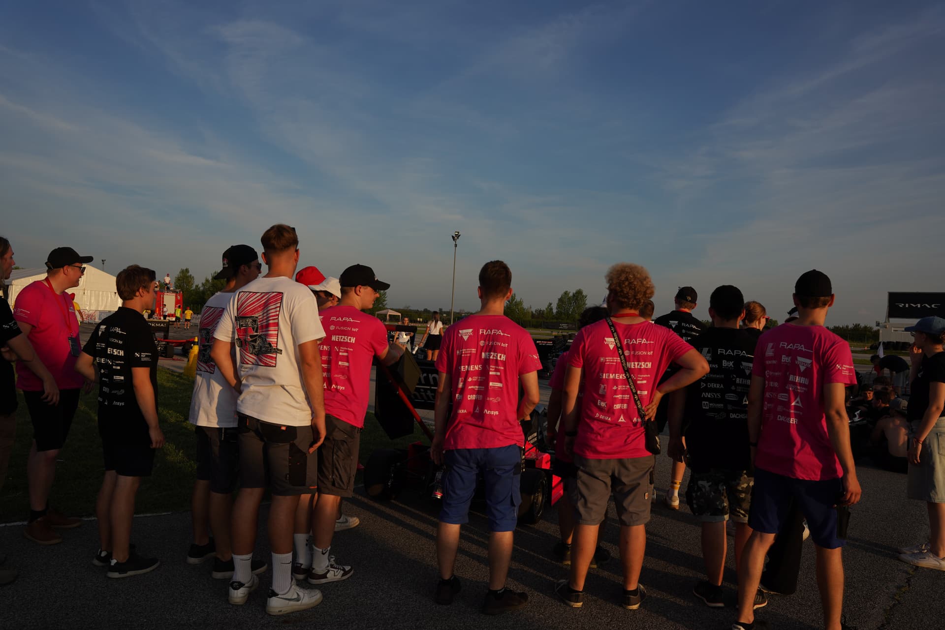 Rückenansicht des Teams in Teamkleidung, aufgestellt hinter dem Rennwagen Artemis